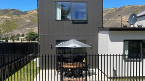 A modern two-story house with a patio area featuring a table and chairs, a satellite dish, and a view of a mountainous landscape.