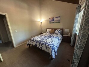 Une chambre à coucher avec un lit, une table de chevet, une lampe, un tableau au mur et une porte.