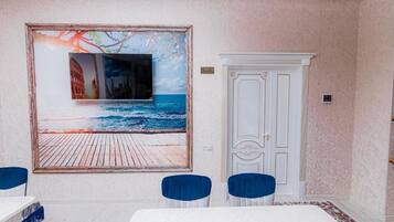Una habitación con un cuadro grande de una escena costera, una puerta blanca y dos sillas azules.