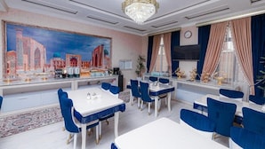 A dining area with a large painting, blue chairs, and a chandelier.