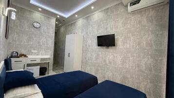 A hotel room with two beds, a desk, a TV, and a clock on the wall.