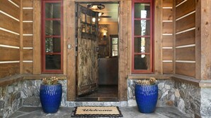 A wooden cabin entrance with a stone foundation, a wooden door with a red frame, and two blue vases on either side. - 2,500 Sq Ft Cabin | 2 Living Rooms | BBQ (South Lake Tahoe)