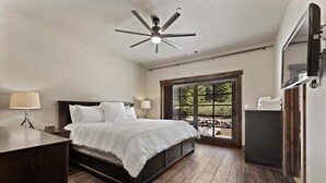 A bedroom with a bed, a ceiling fan, a TV, and a window with a view of greenery. - 2,500 Sq Ft Cabin | 2 Living Rooms | BBQ (South Lake Tahoe)