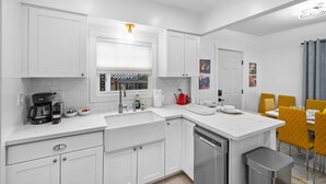 Una cocina moderna con armarios blancos, lavavajillas integrado y una zona de comedor con sillas amarillas.
