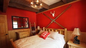 Une chambre avec un lit en bois, des murs rouges, une tête de lit en bois, un miroir, une table de chevet avec une lampe et un motif représentant une piste de ski de cross sur le mur.