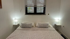 A bedroom with a double bed, two bedside lamps, a window with blinds, and a wall socket. - Pleasant Apartment With Pool (Porec)