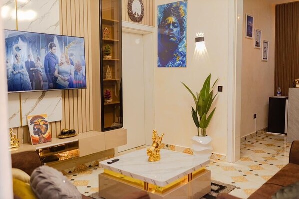 Relax in style with a comfortable sofa, flat-screen TV, and elegant coffee table, surrounded by a potted plant and decorative shelf.