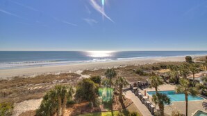 A beach resort with a swimming pool, palm trees, and a view of the ocean.