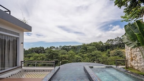A modern outdoor pool area with a view of lush greenery and a stone wall. - Royal Urban Resort (Caringin)