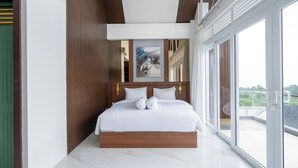 A modern bedroom with a large bed, wooden headboard, and a view of the outdoors through large windows. - Royal Urban Resort (Caringin)