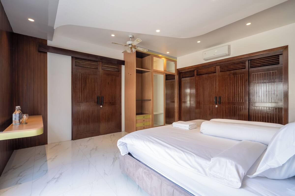 A bedroom with a large bed, wooden wardrobe, and a ceiling fan.