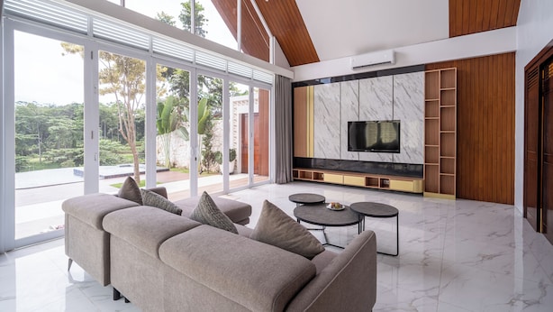 A modern living room with a large sofa, two round coffee tables, and a flat-screen TV against a marble wall. - Royal Urban Resort (Caringin)