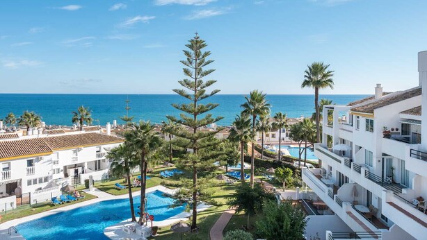 A resort with a swimming pool, palm trees, and a view of the ocean.