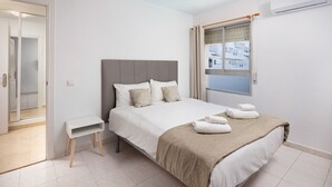 A neatly arranged bedroom with a bed, bedside table, and a window with a view of buildings.