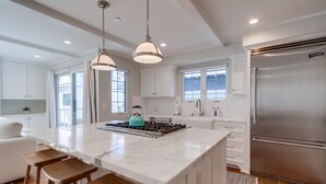 Une cuisine moderne avec des meubles blancs, un grand îlot central doté de tabourets, des appareils en acier inoxydable et un éclairage suspendu.