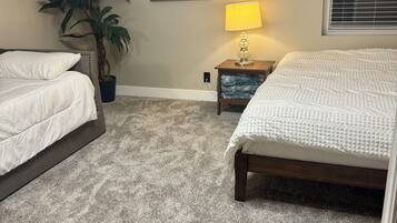 A bedroom with two beds, a large potted plant, a bedside lamp, and a painting on the wall.