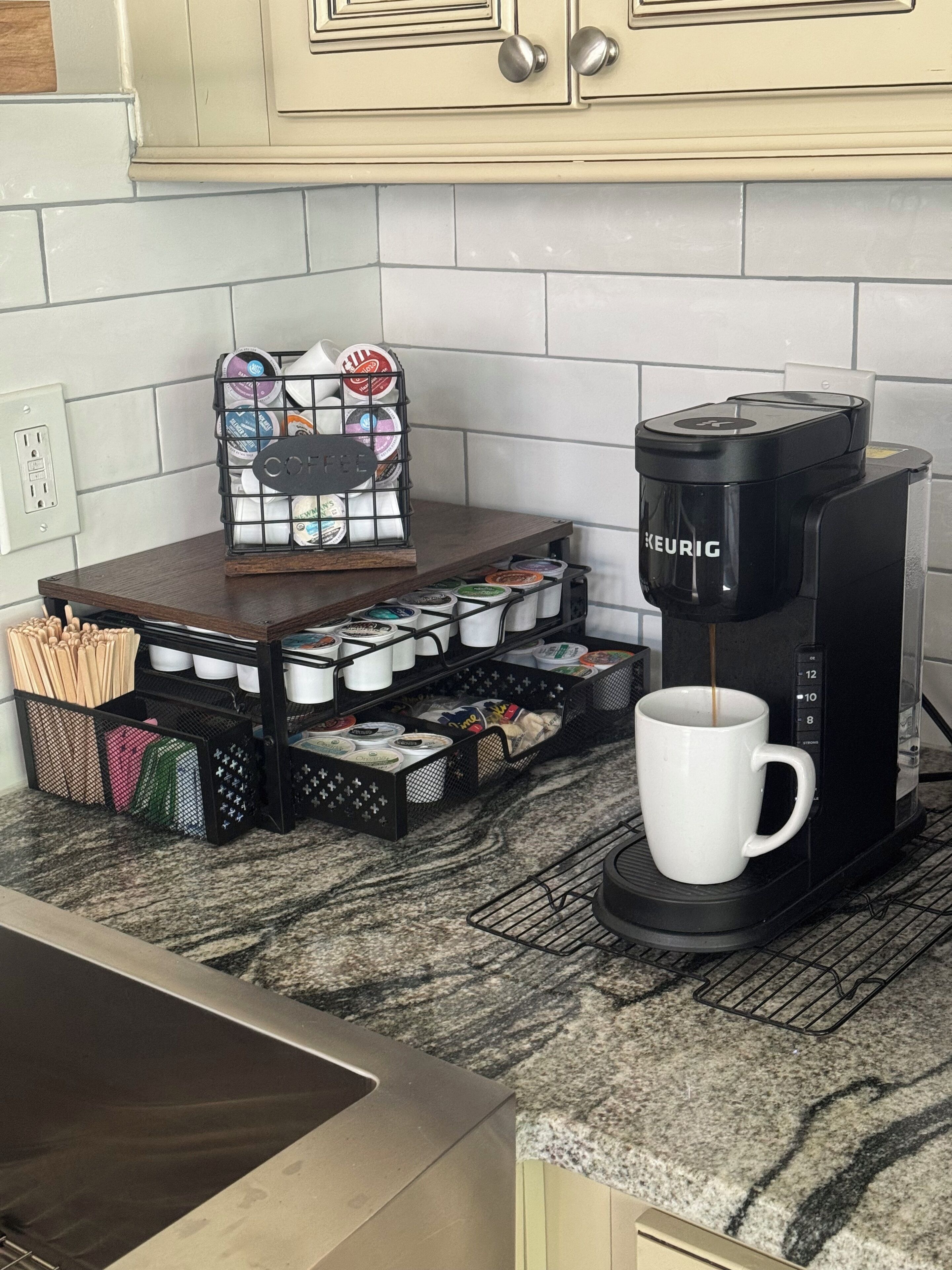 Eine Kaffeemaschine auf einer Küchenarbeitsplatte mit einer Tasse, Kaffeekapseln und einem Kaffeemühle.
