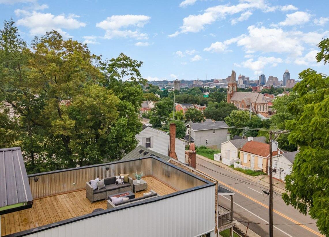 Une terrasse sur le toit, avec un canapé et une table à manger, d’où l’on peut admirer une rue bordée de maisons et, au loin, le panorama de la ville.