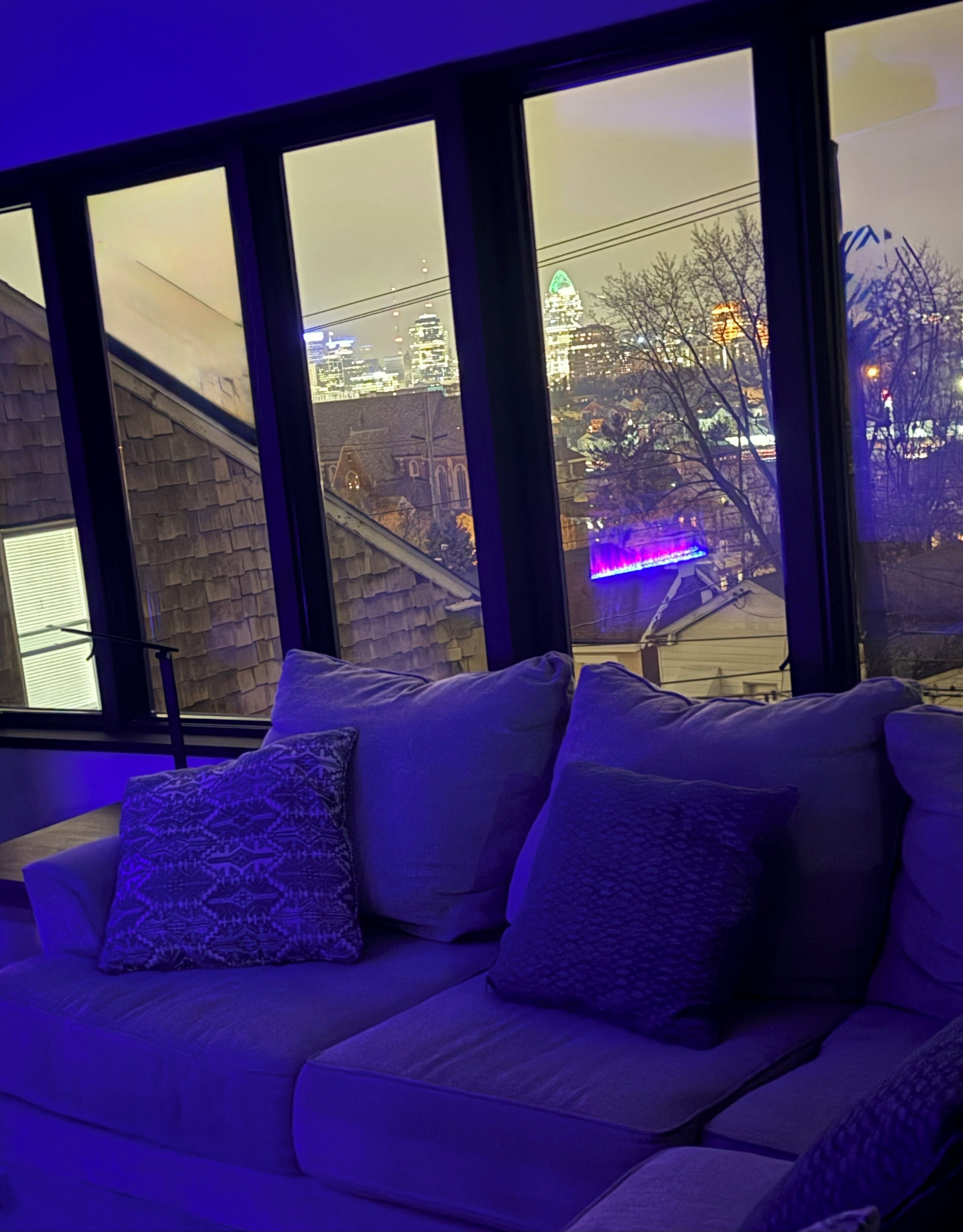 Ein modernes Wohnzimmer mit einer Couch und großen Fenstern mit Blick auf eine Skyline.