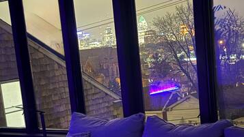 Ein modernes Wohnzimmer mit einer Couch und großen Fenstern mit Blick auf eine Skyline.