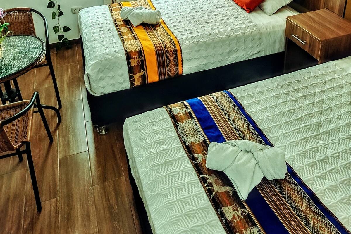 Quarto de hotel com duas camas, uma mesinha e uma cadeira.