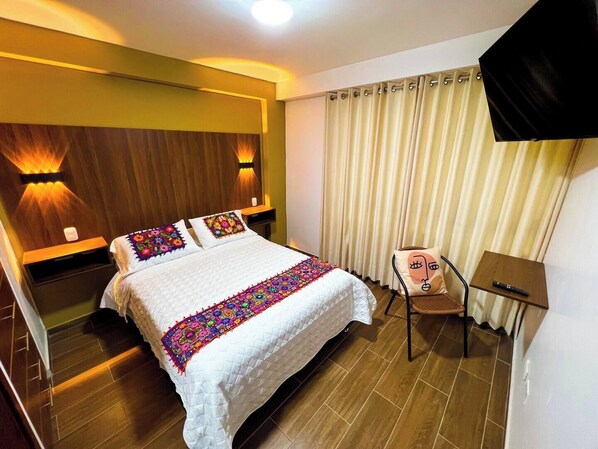 A hotel room with a bed, a chair, a desk, and a TV.