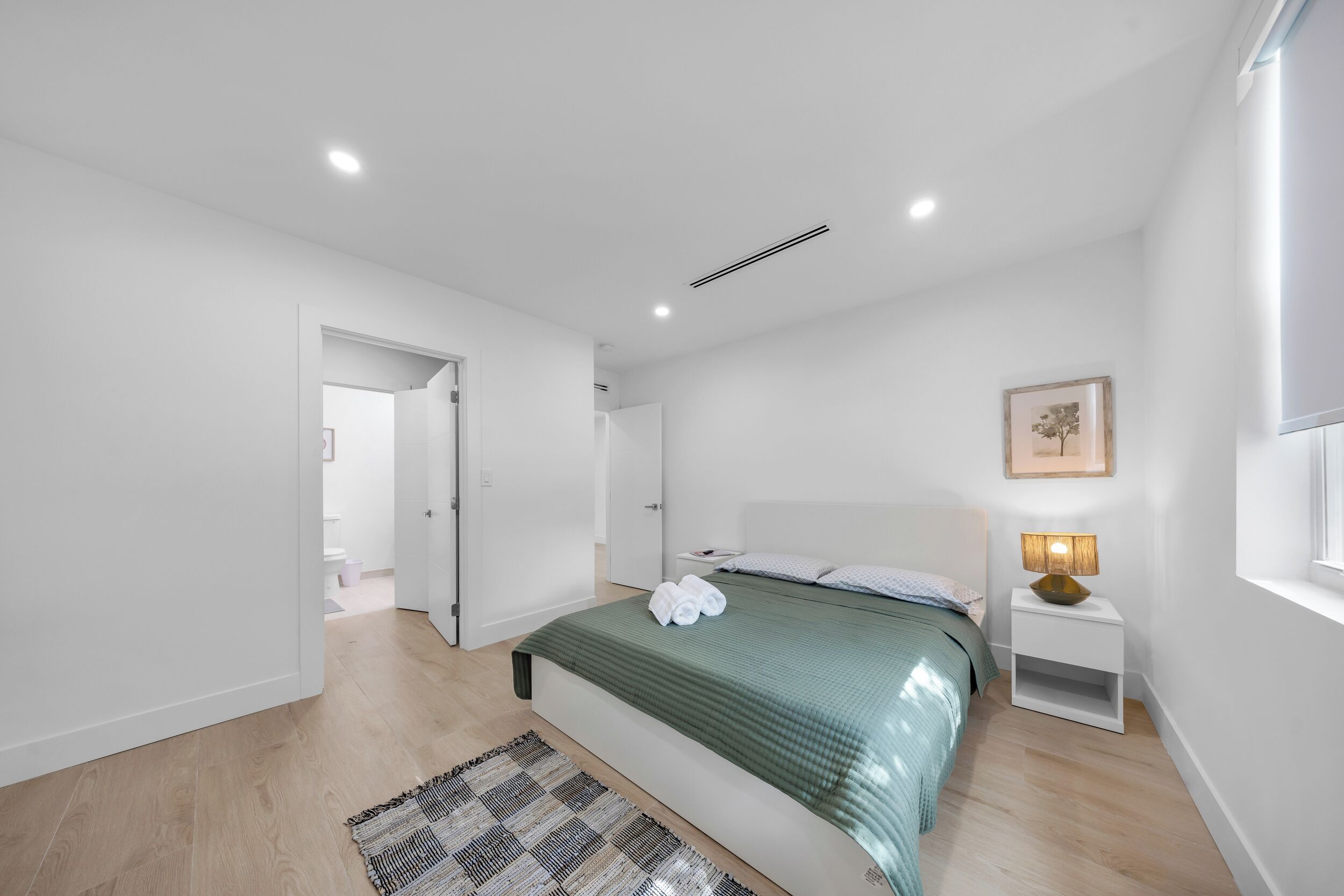 A modern bedroom with a bed, bedside table, and a nightstand with a lamp.