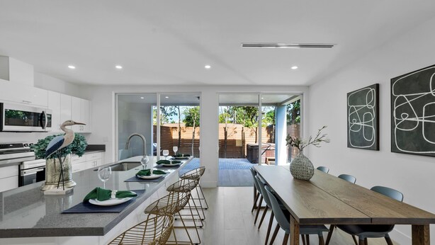 A modern kitchen with a central island, a dining area with a wooden table and chairs, and a view of the backyard through glass doors. - Up to 12 guest Modern Villa near Wynwood! (Miami)