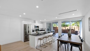 A modern kitchen with a central island, stainless steel appliances, and a dining area with a wooden table and bar stools. - Up to 12 guest Modern Villa near Wynwood! (Miami)