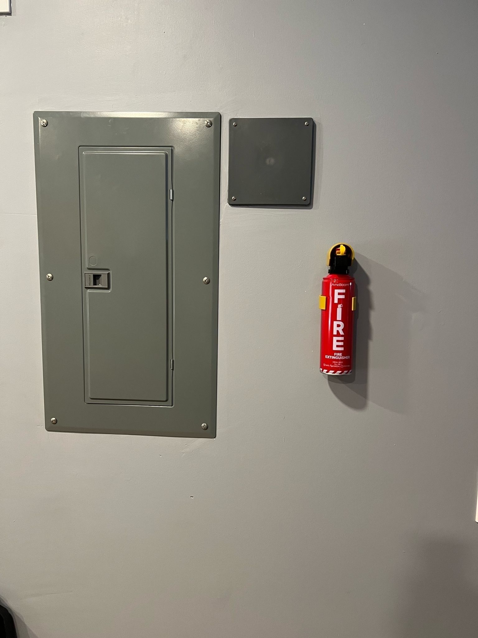 Uma porta cinzenta com um extintor preso na parede ao lado.