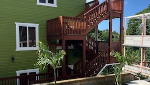 Un edificio verde con una escalera de madera que conduce a un balcón. Hay dos plantas pequeñas en macetas de concreto.
