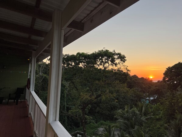 A balcony with a view of the sunset over a forested area.