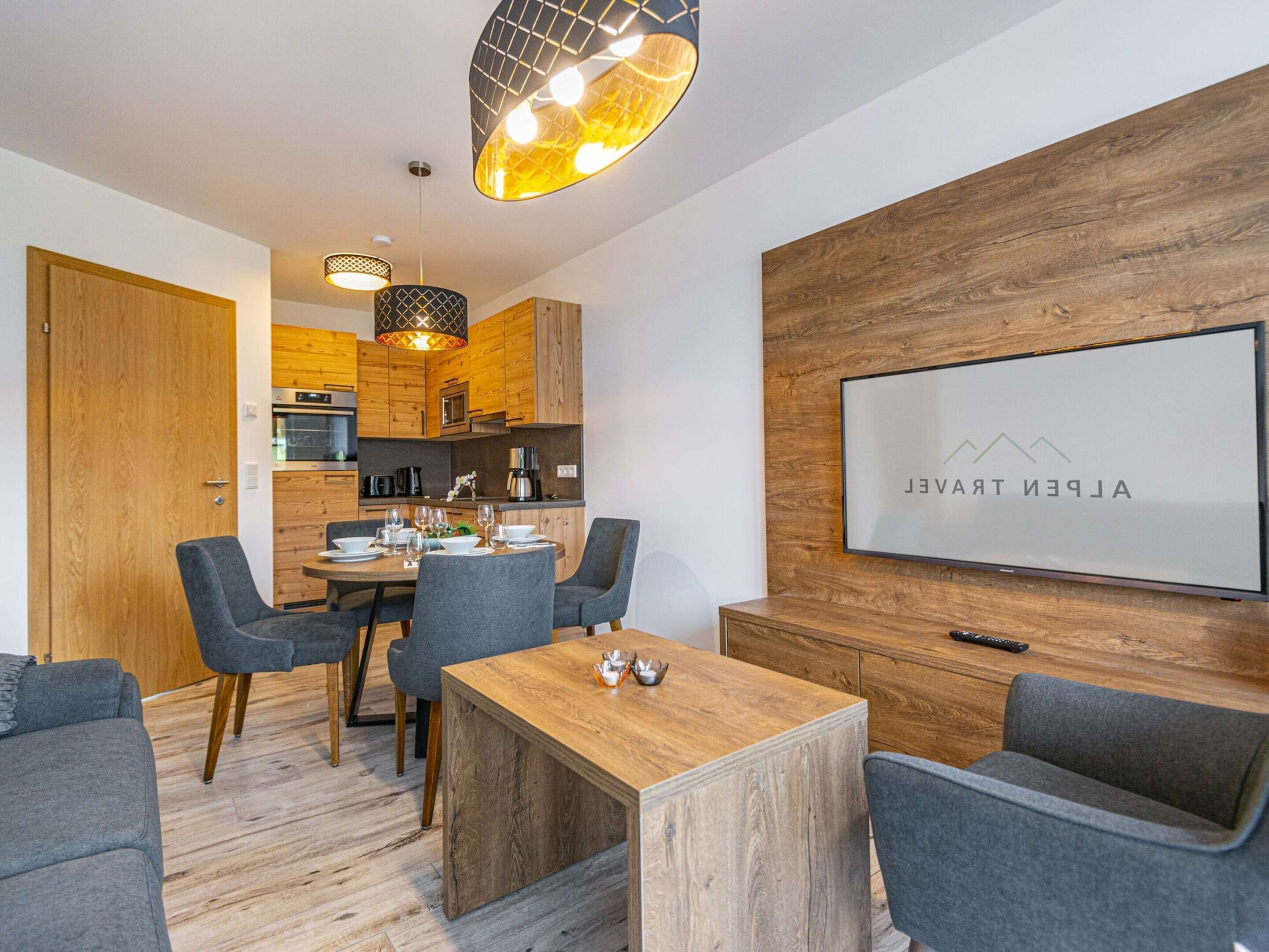 A modern living room with a wooden dining table, grey sofas, and a TV mounted on a wooden wall.