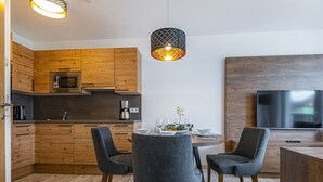 Een moderne keuken met houten kastjes, een eethoek met grijze stoelen, een ronde tafel en een aan de muur bevestigde televisie.