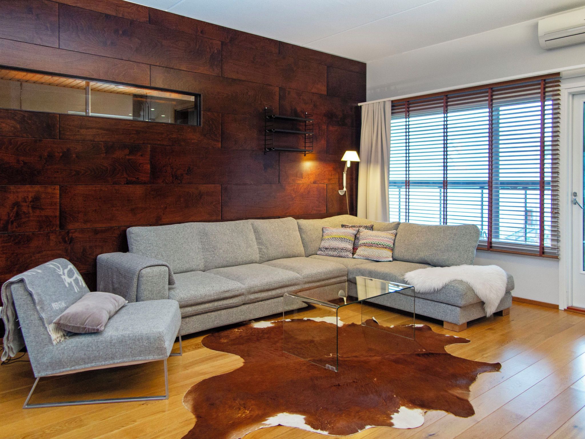 A modern living room with a sectional sofa, a glass coffee table, and a large brown and white cowhide rug.