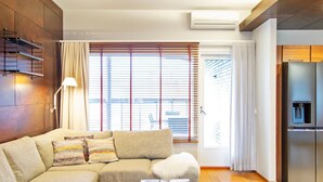 Una sala de estar moderna con un sofá seccional, una mesa de centro de vidrio, piso de madera y un ventanal con persianas.