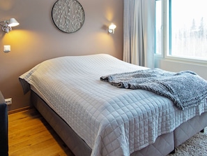 Een slaapkamer met een bed, een wandlamp en een raam met gordijnen.