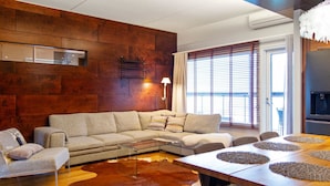 Una sala de estar moderna con una pared de madera, un sofá modular, una mesa de centro de vidrio y una mesa de comedor con individuales.