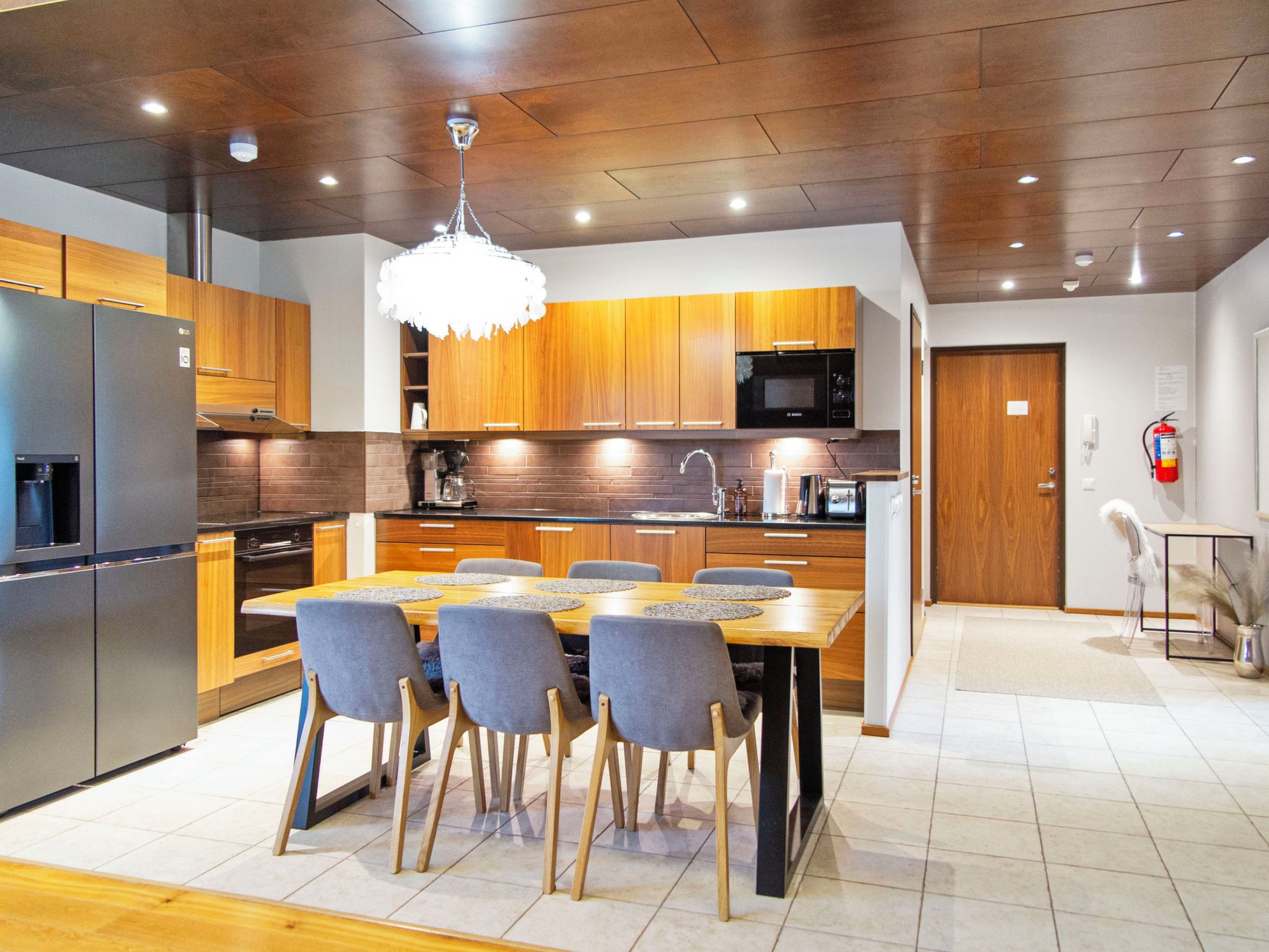 A modern kitchen with wooden cabinets, a stainless steel refrigerator, a microwave, and a dining area with a table and chairs.