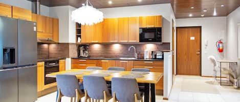 A modern kitchen with wooden cabinets, a stainless steel refrigerator, a microwave, and a dining area with a table and chairs.
