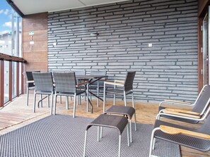 An outdoor seating area with wicker chairs and a table, a stone wall, and a wooden deck.