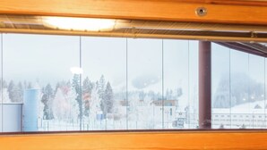 Vista a través de una ventana con marco de madera, que da a un paisaje nevado con árboles y edificios.