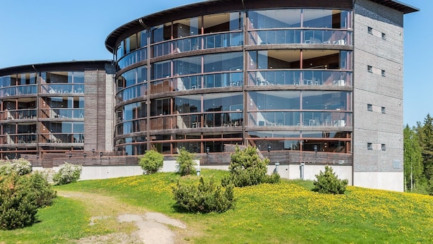Un edificio moderno de varios pisos con fachada curva, grandes ventanales de vidrio y una combinación de materiales de madera y metal.