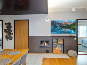 Een moderne woonkamer met een open haard, een groot flatscreen televisietoestel dat erboven is bevestigd, en een houten eettafel met een placemat.