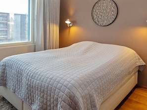 A neatly made bed with a quilted blanket, a wall-mounted light fixture, and a window with blinds. - Tahko spa suites white b 7 by Interhome (Nilsiä)