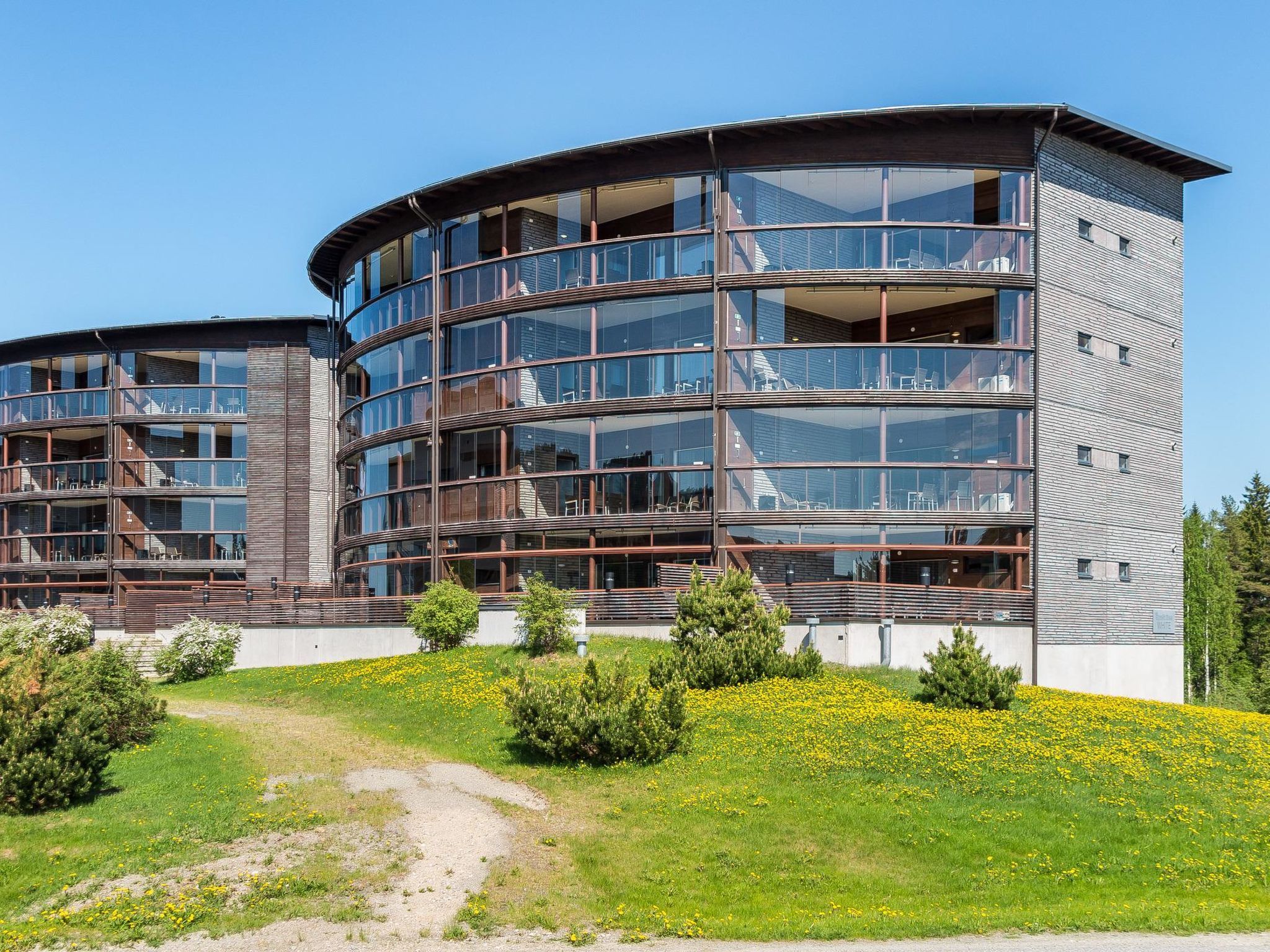 A modern multi-story building with a curved facade, large glass windows, and a mix of wooden and metal materials.