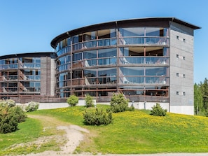 A modern multi-story building with a curved facade, large glass windows, and a grassy area with yellow flowers in front.