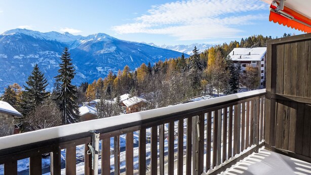 Ein Balkon mit Blick auf schneebedeckte Berge und Herbstbäume.