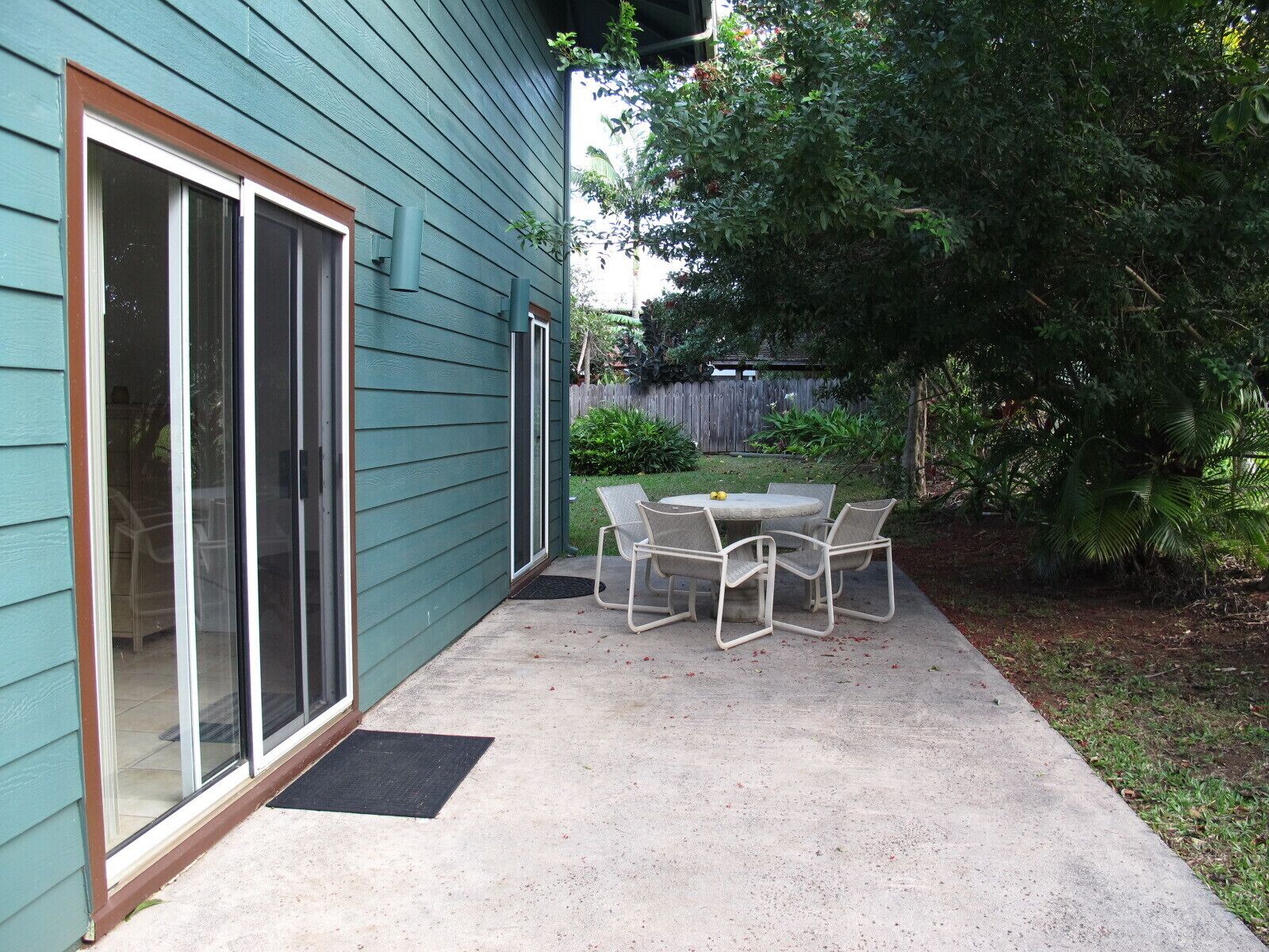 Um pátio com mesa e cadeiras, uma porta de vidro deslizante e fachada verde.