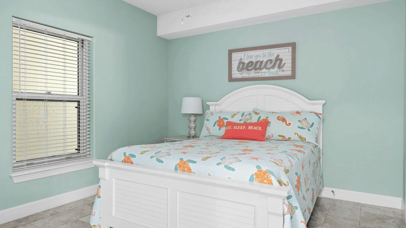 A bedroom with a bed, a window with blinds, a bedside table, and a wall decoration.